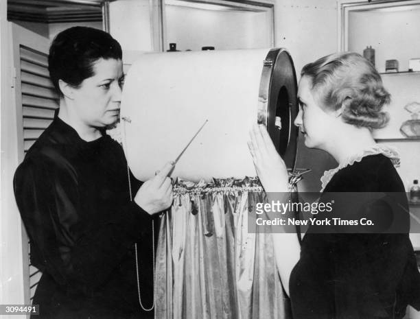 Beautician operates a facial line detector invented by Helena Rubinstein. The device contains a number of powerful lenses and is used to detect...
