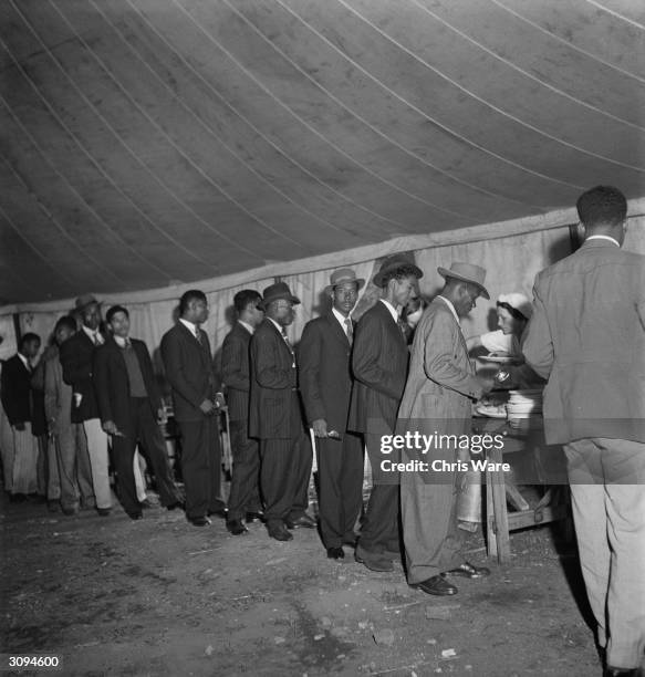 Jamaican men, who arrived in Britain on HMT Empire Windrush on 22nd June, line up in a canteen marquee on Clapham Common to get a meal, London, June...