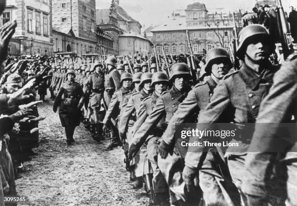 Steel helmeted German troops marching into Prague during the invasion of Czechoslovakia. By-standers are giving them a Nazi salute.