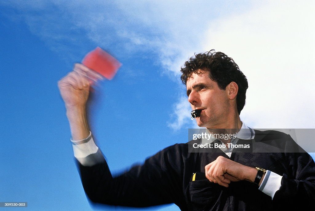 Football referee holding up red card, blowing whistle, close-up