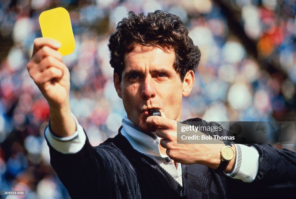 Football referee blowing whistle & holding up yellow card (Composite)