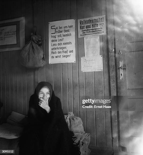 An old woman sits amidst her belongings in post-war Vienna. Above her a sign offers 'Advice and Assistance' to German people.