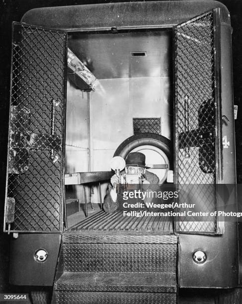 Polish born American photographer Weegee takes a photograph from the interior of a police van.