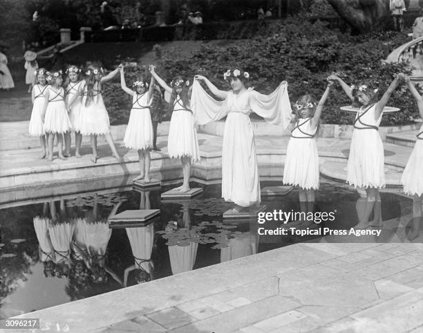 Dancers in 'grecian' costume stand on stepping stones across a lily pond at a Hampstead Garden Fete.