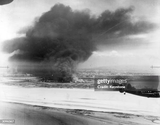 Coastal Command Lockheed Hudson flying past burning oil tanks on Dunkirk beach.