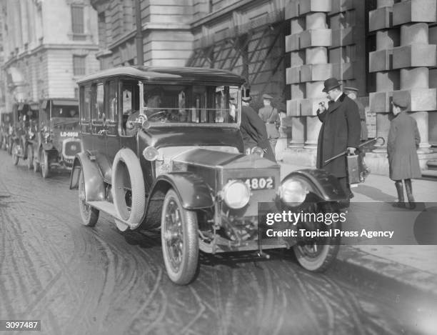 Lord Derby stands on the pavement by the side of a Rolls-Royce.