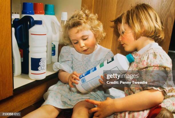 two girls (2-3) in home, examining bottle of bleach - toxin stockfoto's en -beelden