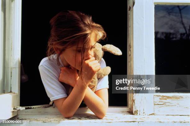 girl(7-8)hugging cuddly toy,sucking thumb,leaning out of rotting windo - kindermishandeling stockfoto's en -beelden