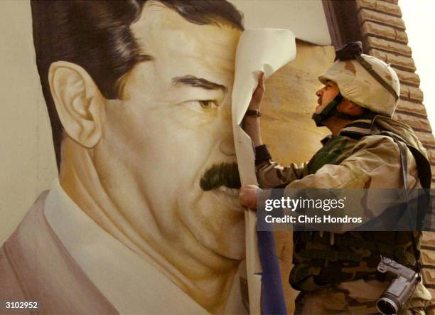 Marine Major Bull Gurfein pulls down a poster of Iraqi President Saddam Hussein March 21, 2003 in Safwan, Iraq. Chaos reigns in southern Iraq as...