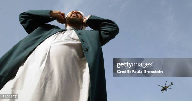 An Iraqi Sunni Muslim cleric holds his ears while looking towards the sky as a U.S military helicopter goes by during an anti-U.S. Demonstration in...