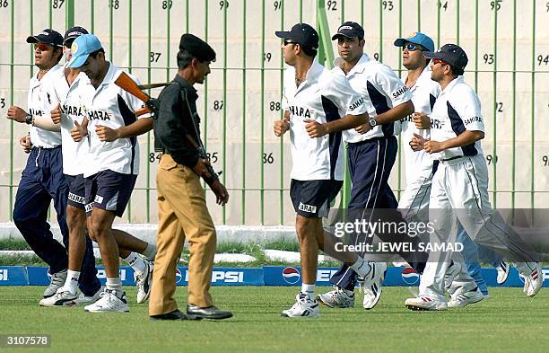 An armed Pakistani policeman looks at members of the Indian cricket team as they jog during a practice session at the Arbab Niaz Stadium in Peshawar,...