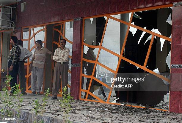 Iraqis stand in front of the smashed front screen of a hotel in Iraq's main southern city of Basra following a carb bomb explosion 18 March 2004,...
