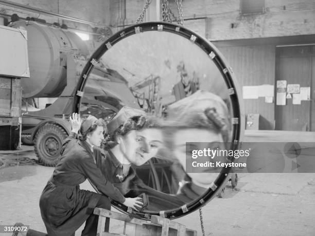 Mrs Kathleen Would catches a warped reflection of herself as she polishes one of the giant reflectors at a searchlight factory in the Midlands during...