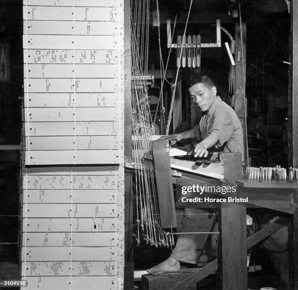 Weaver at work on one of the Jacquard hand looms at a Nishijin plant in Kyoto. Perforated patterned cards determine the woven design. Rows of bobbins...
