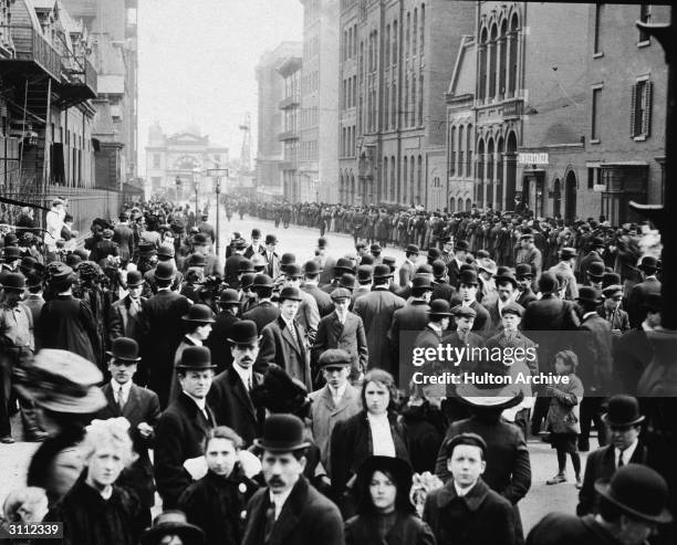 Crowds of people stand in the street, waiting to identify bodies of immigrant workers following the Triangle Shirtwaist Company fire in New York...