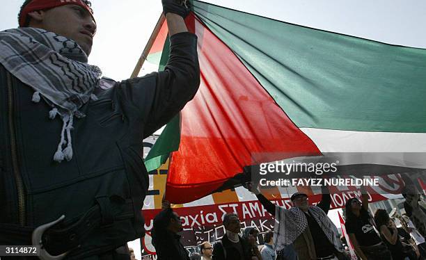 Palestinian protesters hold up a huge national flag in front of the US embassy as they attended a demonstration against war to mark the one year...