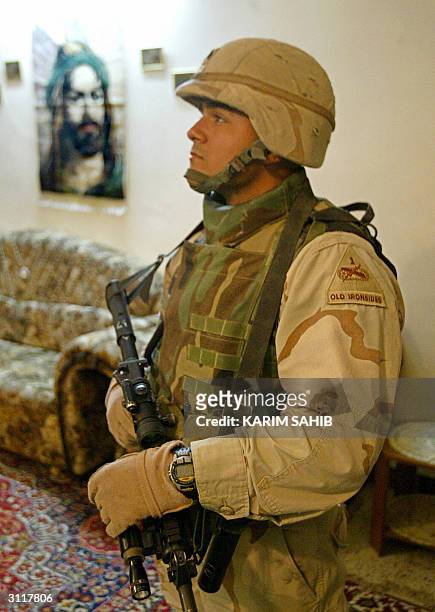 1st Cavalry soldier stands on guard, with a portrait of Prophet Mohammed's cousin and son-in-law Imam Ali in the background, as his comrades search a...