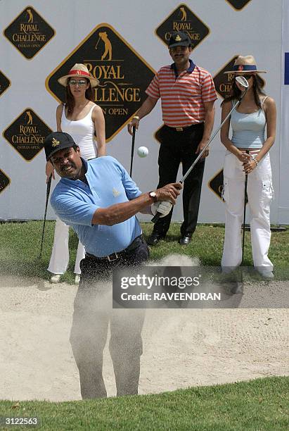 Former Indian Cricket captain Kapil Dev tees off as Indian models Aditi Govitrikar and Surthi Sharma look on during the opening day of the Royal...