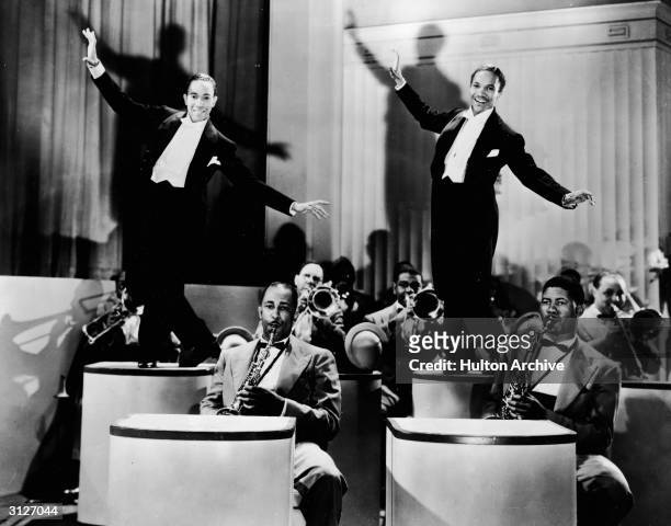 American tap dancing duo The Nicholas Brothers, featuring Harold and Fayard, perform on two pedestals, backed by an orchestra in an unidentified film...