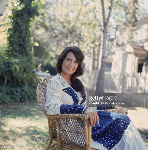 Portrait of American country music singer and guitarist Loretta Lynn as she sits outside in a chair, 1970s.