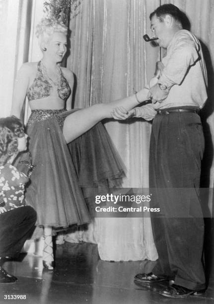 Kenny Williams, the dance director at the 20th Century Fox studios, relieves a touch of cramp in one of Betty Grable's famous legs. Ms Grable is...
