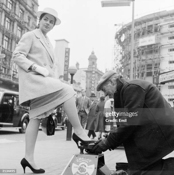 British starlet Gale Sheridan has her shoes polished by a shoeshine in Leicester Square, London. She is wearing a three-quarter length jacket and a...