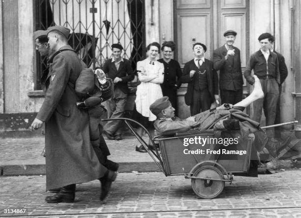 Wounded German officer captured during the liberation of Cherbourg is dragged along in a handcart, to the amusement of onlookers.