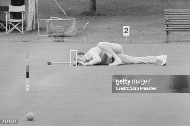 Player contorts his body in order to get a good view through the hoop at an open croquet championship.