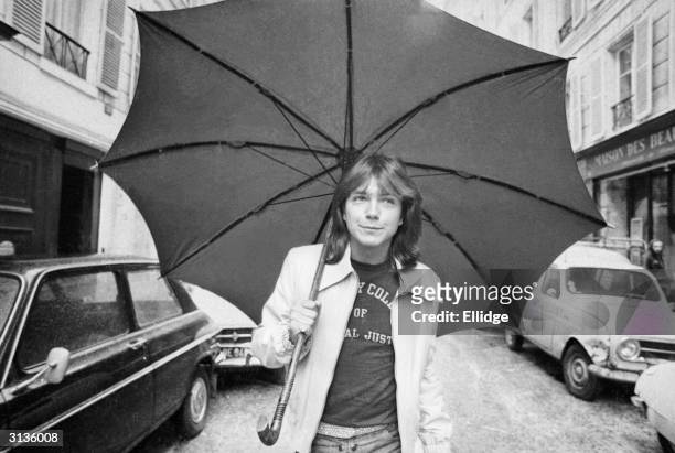 David Cassidy, American pop singer and star of the television programme 'The Partridge Family', walking down a road in Paris with an umbrella, 30th...
