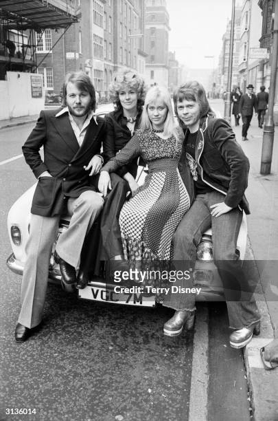 Benny Andersson, Anni-Frid Lyngstad, Agnetha Faltskog and Bjorn Ulvaeus of the Swedish pop group ABBA sitting on the bonnet of a sports car.