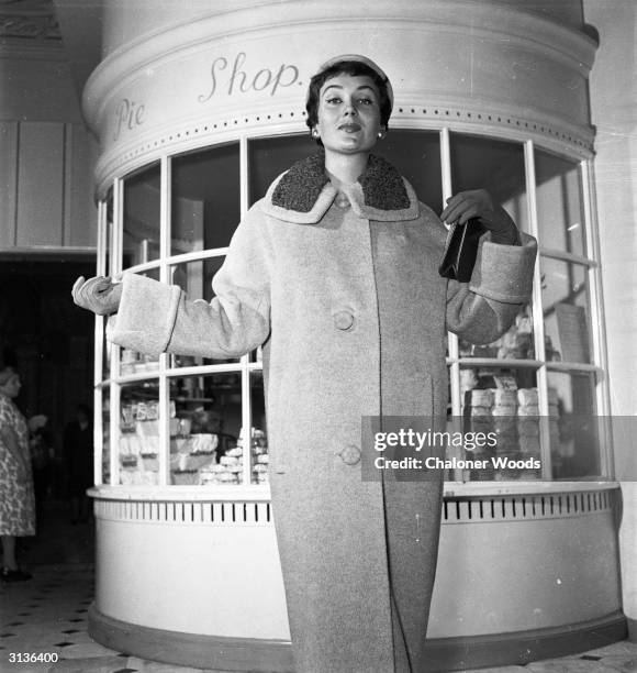 Lady standing by the pie shop in Harrods department store, London, wearing a long buttoned coat.