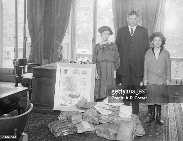 American Statesman Herbert Hoover ; closely associated with relief of distress in Europe he is standing with his wife and daughter by a poster...