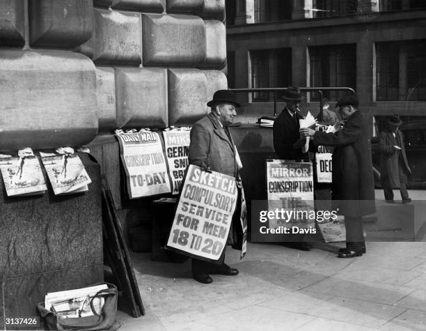 Newspaper placards in London announce the conscription of all men aged 20 and 21 into the army, with exemptions solely on medical grounds. The men...