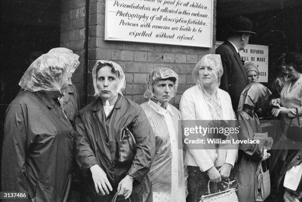 Group of ladies in waterproof hats queuing in the rain outside Ascot.