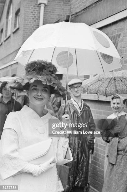 Woman with an extravagantly decorated hat and a spotted umbrella on her way to Ascot.