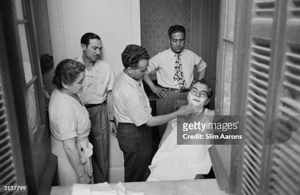 Premium Rates Apply. 1949: Sicilian born American gangster, Charles 'Lucky' Luciano being watched by his entourage as he is given a shave while...