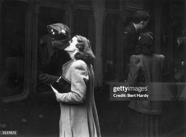 Soldier leans out of a carriage window to kiss his wife goodbye at Paddington station in London. Original Publication: Picture Post - 1133 - War-Time...