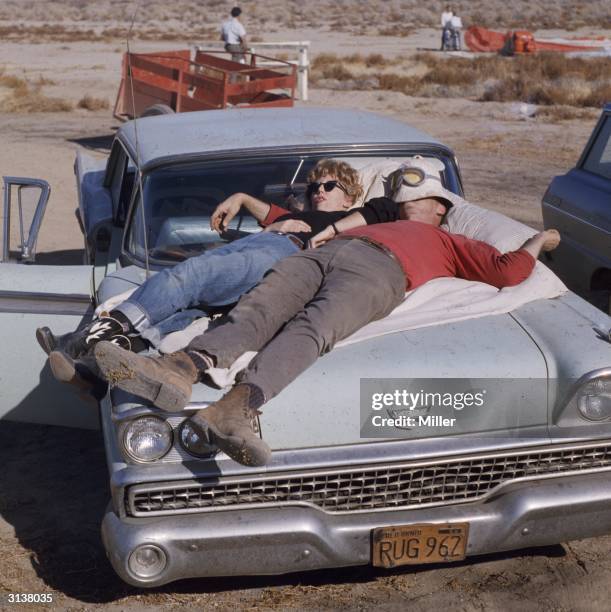 Couple sleeping on the bonnet of their car during a hot air balloon show in the desert.