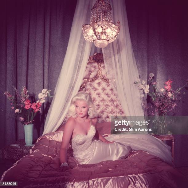 Film star Diana Dors in blonde bombshell pose on a satin covered bed.