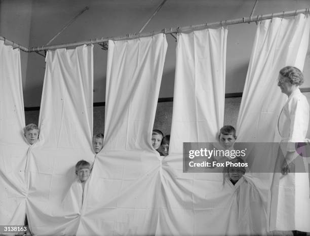 Young boys peering through cubicle curtains at the Open Air Recovery School in Kettering, Northants.