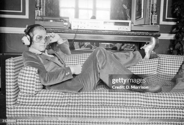 English pop star Elton John relaxes on a sofa and listens to some music.