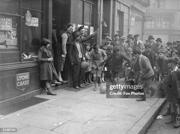 Boys playing football along the pavement watched by a crowd in 'Little Italy', Clerkenwell, London in anticipation of an International match between...
