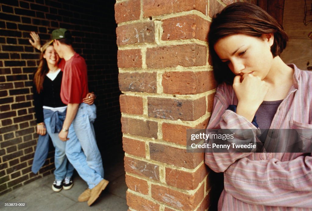 Teenagers (15-17), girl with sad expression, couple in background