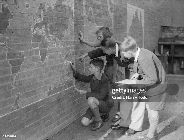 Pupils at Aspen Open Air School in Streatham Hill, London plot the Duke of Gloucester's route to Australia on a map painted on the wall of their...