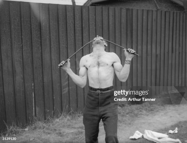 Strong man, George Challard of Woowich, London who can bear the weight of a car on his neck shows he can bend an iron bar with his teeth.