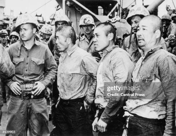 Three Japanese prisoners of war surrounded by American soldiers after they were captured during fighting on Iwo Jima.