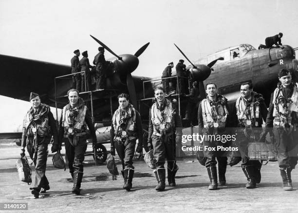 The crew of a Lancaster bomber walk away from their plane after a flight while ground crew check it over.