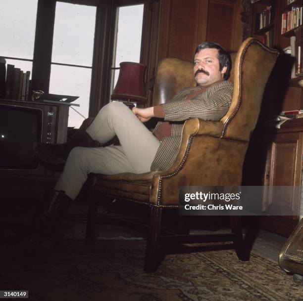 British actor Oliver Reed relaxes in an armchair in his huge ex-monastery home, Broome Hall, near Dorking in Surrey.