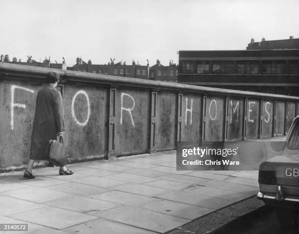 Woman carrying a shopping bag walks past graffiti on the iron bridge on Rossmore Road in Marylebone arguing that disused land owned by British...