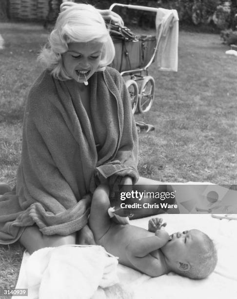 Holding a safety pin between her teeth like any other mother, American sex symbol Jayne Mansfield changes the nappy of her son Miklos Hargitay in the...